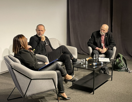 Prelegenci: dwa mężczyźni i kobieta siedzą przy stoliku i rozmawiają.