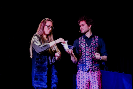 Kobieta wyjmuje ze szklanego pojemnika kartę. Naczynie trzyma magik.