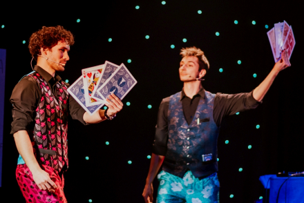 Zbliżenie na twarze magików, którzy wymachują wachlarzami z kart.