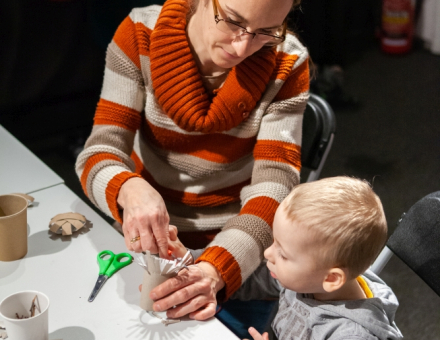 Chłopiec z mamą siedzą przy stole i robią świąteczną ozdobę z rolki po papierze toaletowym.