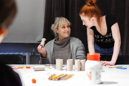 Dwie kobiety robią ozdoby świąteczne. Przed nimi na stole leżą rolki po papierze toaletowym.