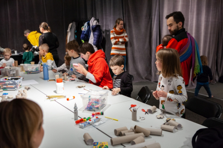 Grupa dzieci i rodziców pracuje przy stoliku. Robią ozdoby świąteczne z rolek po papierze toaletowym.