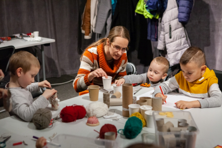 Trzech chłopców oraz kobieta robią renifery z rolek po papierze toaletowym.