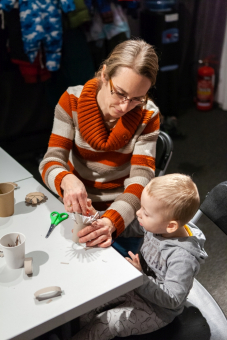 Chłopiec z mamą siedzą przy stole i robią świąteczną ozdobę z rolki po papierze toaletowym.