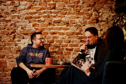 Prowadzący spotkanie przygląda się Jarkowi Szubrychtowi, który mówi do mikrofonu.