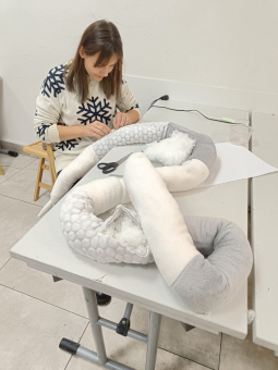 Kobieta siedzi przy stole i kończy zszywać swojego węża.