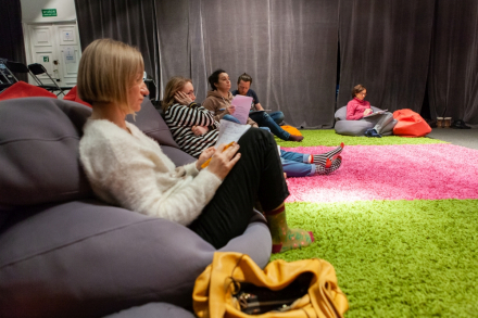 Uczestnicy spotkania siedzą na pufach i robią notatki.