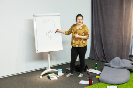 Prowadząca warsztat rysuje coś na tablicy. Dookoła niej rozsypane są kartki.