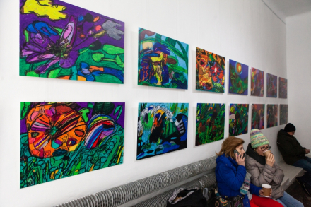 Trzy osoby siedzą na ławce pod obrazami artysty.