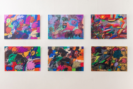 Sześć kolorowych obrazów zawieszonych na ścianie w holu Warsztatów Kultury.