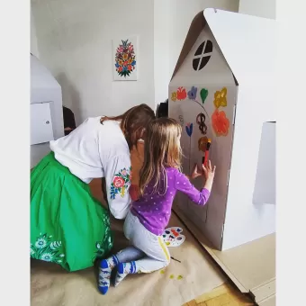 Kobieta i dziewczynka malują drzwi kartonowego domku.