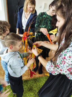 Kobiety i dzieci ozdabiają gałąź wstążkami.