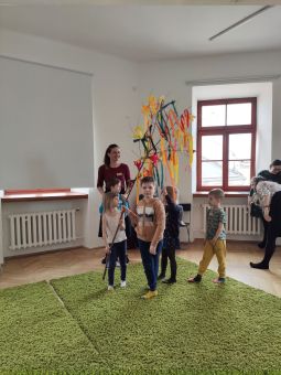 Dzieci trzymają gałąź z zawieszonymi kolorowymi wstążkami.