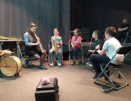 Dzieci grają na instrumentach, siedząc na krzesłach w półkolu.