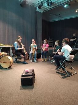 Dzieci grają na instrumentach, siedząc na krzesłach w półkolu.