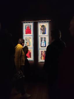 Osoby oglądają dwie, pionowo zawieszone kolumny obrazków, wokół panuje półmrok.
