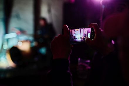 Zbliżenie na dłonie dziewczyny, która trzyma w ręce telefon i robi zdjęcie zespołowi.