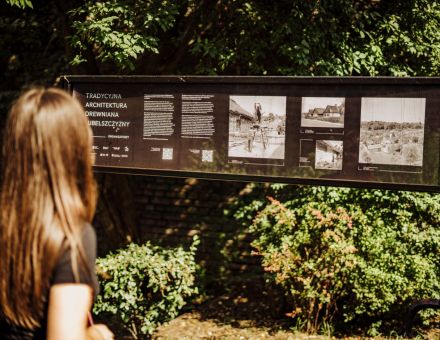 Kobieta ogląda wystawę zdjęć  na podłużnym stojaku.