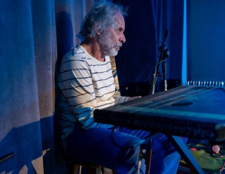 Mężczyzna gra na dużym instrumencie strunowym, który kształtem przypomina pianino.