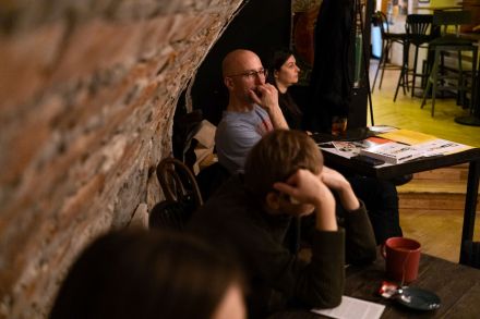 Przy dwóch stolikach siedzą ludzie i słuchają dyskusji