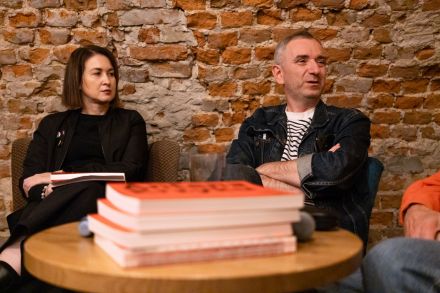 Przy okrągłym stole siedzi kobieta i mężczyzna. Na stole leżą książki.