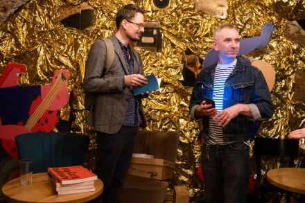 Dwaj mężczyźni stoją na środku pomieszczenia i rozmawiają.