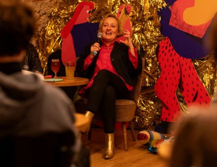 Autorka książki śmieje się do publiczności. W ręce trzyma mikrofon.