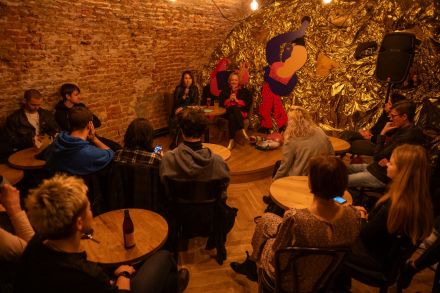 Zdjęcie zrobione z góry. Uczestnicy spotkania siedzą przy stolikach i słuchają autorki książki.