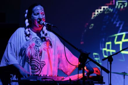 Zbliżenie na twarz wokalistki. Jest ubrana jak indianka i ma pomalowaną twarz.