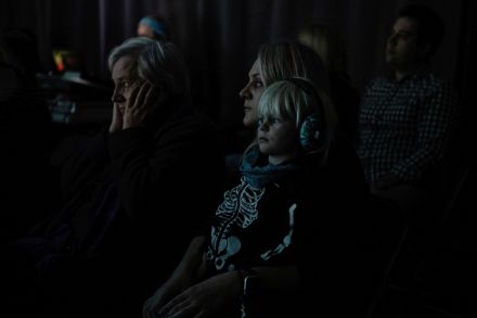 Kobieta trzyma syna na kolanach. W sali jest ciemno.