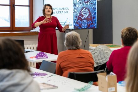 Kobieta stoi przy oknie i prowadzi wykład o wycinankach w Ukrainie.