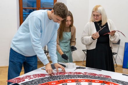 Dwie kobiety i mężczyzna układają ogromną wycinankę z małych kawałków.