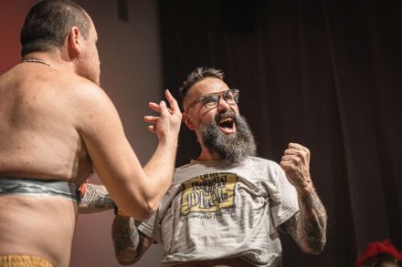 Nagi mężczyzna ma przyklejoną do brzucha taśmę. Stoi przed nim inny mężczyzna.