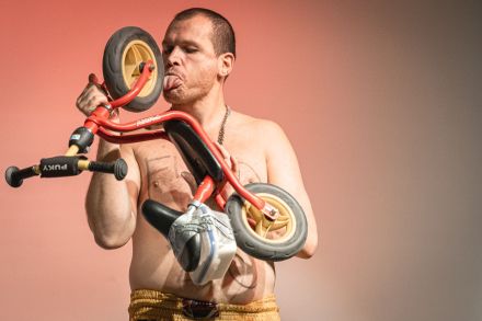 Artysta liże koła od roweru dziecięcego.