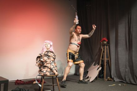 Artysta rozlewa wódkę. Na krześle stoi manekin lalki.
