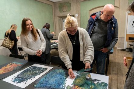 Ludzie oglądają gotowe małe wycinanki, które leżą na stołach.