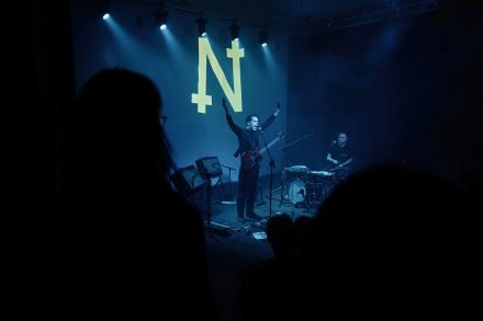 Muzyk, który jest wokalistą  i gitarzystą, stoi z rękami podniesionymi do góry.