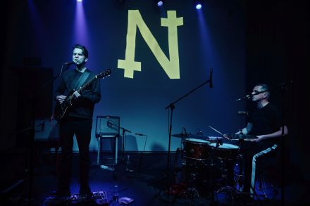 Gitarzysta i perkusista śpiewają. Obaj mają zamknięte oczy.