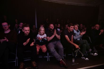 Publiczność siedzi na krzesłach i bije brawo.