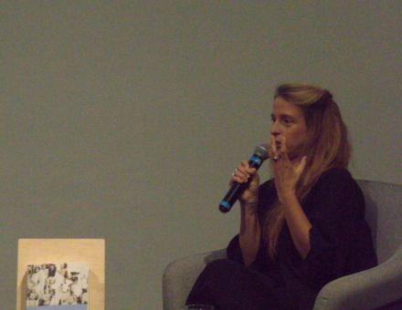 Kobieta w fotelu trzyma mikrofon i opowiada o prezentacji.