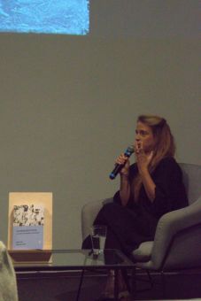 Kobieta w fotelu trzyma mikrofon i opowiada o prezentacji.