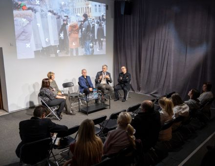 Dwie kobiety i trzech mężczyzn prowadzą debatę. Słuchają ich ludzie, którzy siedzą na krzesłach.