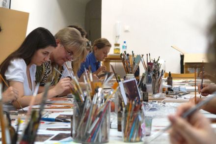 Uczestniczki siedzą przy stole i malują.