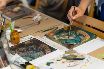 Dłoń kobiety, która trzyma pędzel i coś rysuje na drewnie.