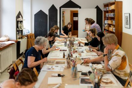 Uczestnicy warsztatów siedzą przy stole i malują.