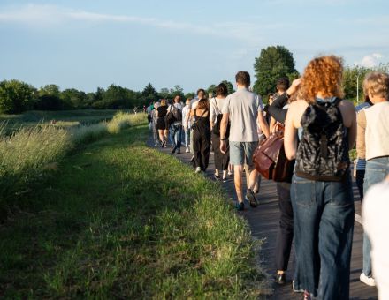 Grupa ludzi idzie drogą między zaroślami. Grupa ludzi idzie drogą między zaroślami.