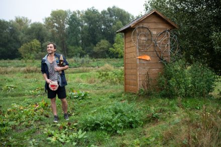 Mężczyzna stoi przy drewnianej chacie, na której są koła z wikliny. Opowiada o swojej pracy.