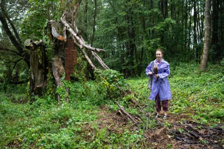 Kobieta stoi przy swojej pracy. To wiklinowy posąg wpleciony w drzewo.