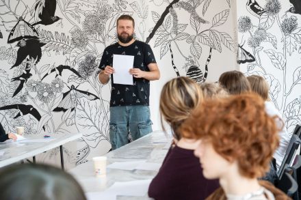 Prowadzący trzyma w ręce kartkę i opowiada coś uczestniczkom.