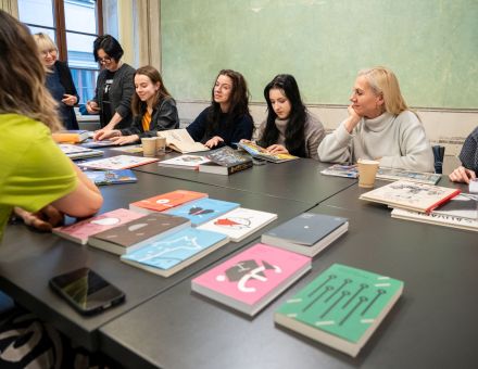 Na stole leżą książki z kolorowymi okładkami. Przy stole siedzą uczestniczki warsztatów.